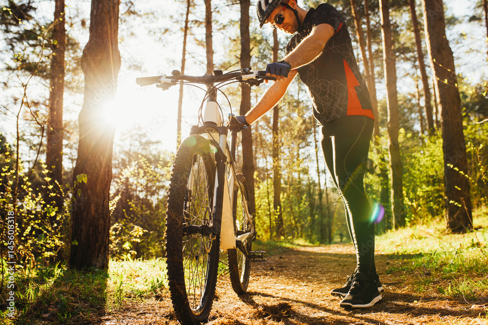Foto Stock Outdoor shot of rider wearing black cycling clothing and  protective gear during workout in woods, preparing his bike to bicycle  before climbing mountain. People, active healthy lifestyle and extreme.