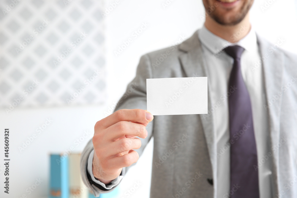 Handsome young man with business card on blurred background, closeup Handsome young man with business card on blurred background, closeup
