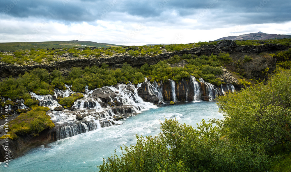 Hraunfossar Wasserfall mit eisblauem Wasser aus Lavafeld in Schlucht mit grünen Bäumen