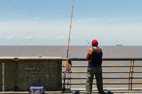 Man fishing in the Rio de la Plata with cargo ship on background