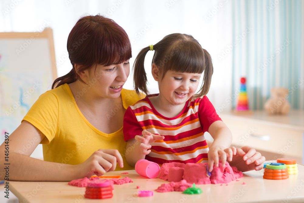 Fototapeta premium A cute little little girl and her mom playing with kinetic sand at home