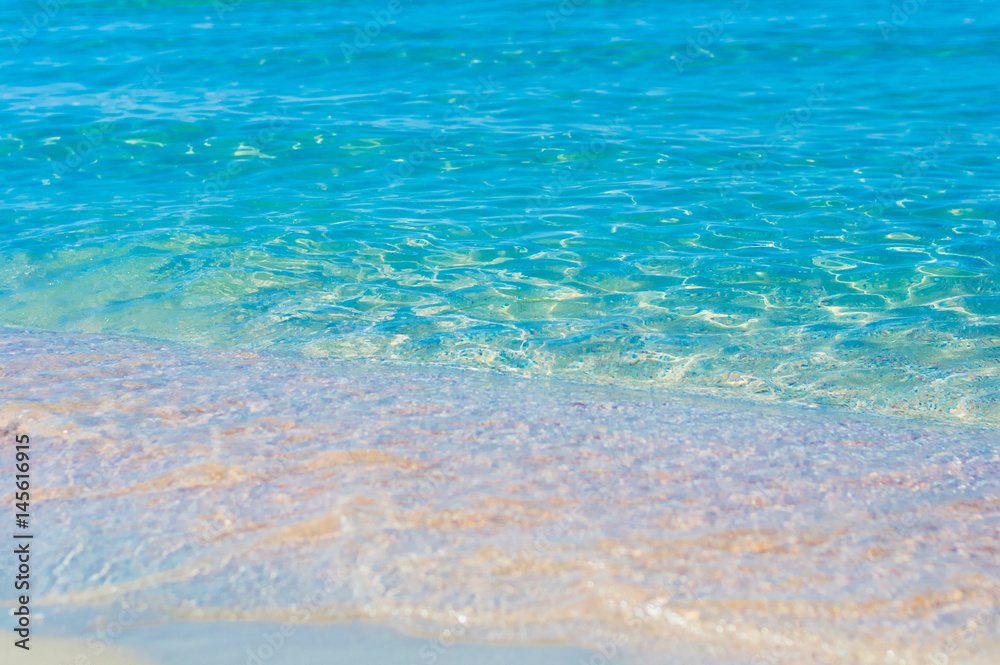 Soft sea waves wash over golden sand in a beach. Blured natural background