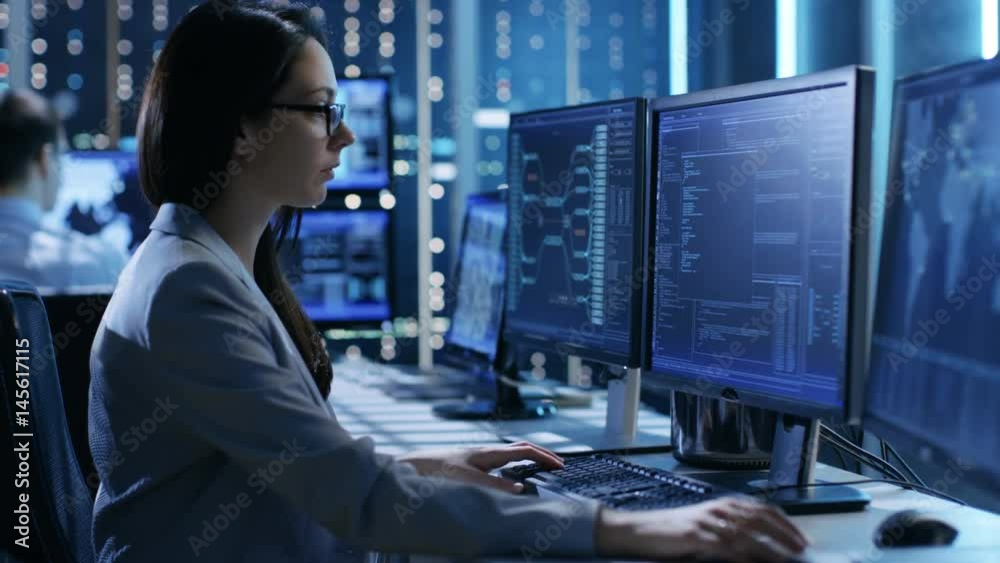 Female System Engineer Controls Operational Proceedings. In the Background People Working and Monitors Show Various Information.  Shot on RED EPIC-W 8K Helium Cinema Camera.