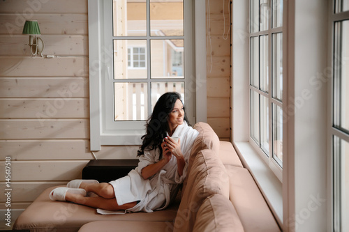 Girl in Bathrobe drinking coffee in the morning on the bed against the window