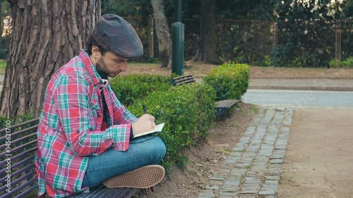 inspired man writes his thougts sitting on a bench at the park  photo