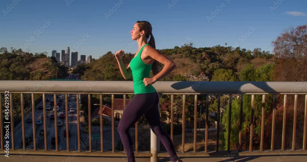 Athletic Woman Working Out. Jogging across a bridge. Trees, Sun and city can be seen in the background. Slow Motion. Athletic Woman Working Out. Jogging across a bridge. Trees, Sun and city can be seen in the background. Slow Motion.