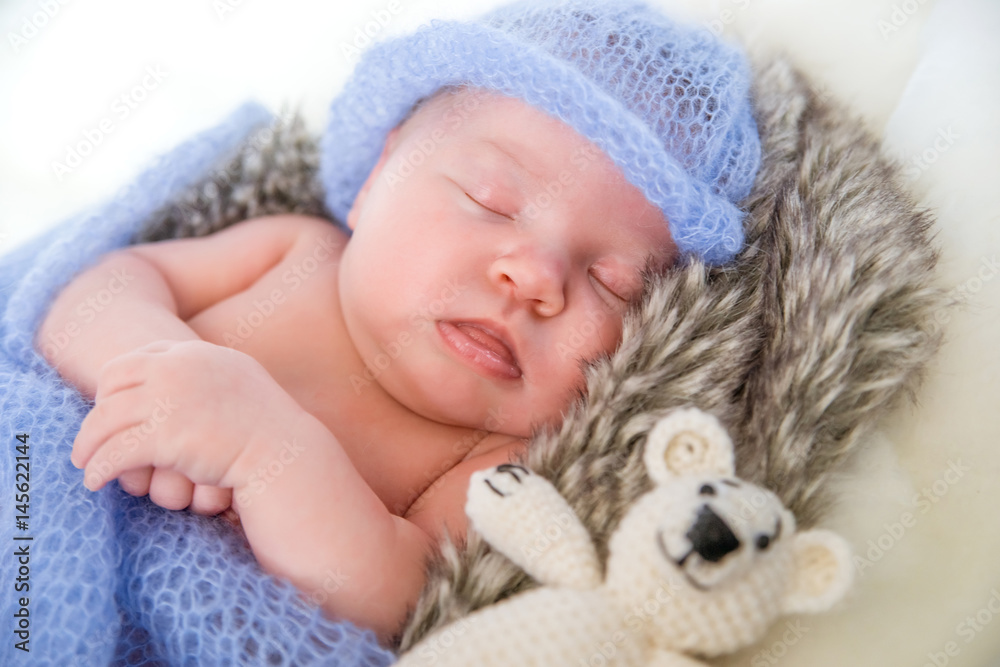 Sleeping newborn baby girl. Newborn baby in knitted cap and with a toy bear lying on a fur blanket. - obrazy, fototapety, plakaty 
