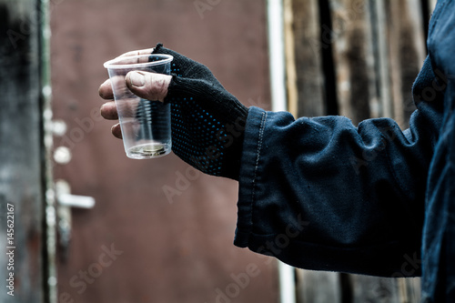 In the man's hand squeezed the plastic Cup. In a plastic Cup are different coins.
