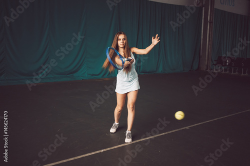 Full body portrait of young girl tennis player in action in a tennis court indoor