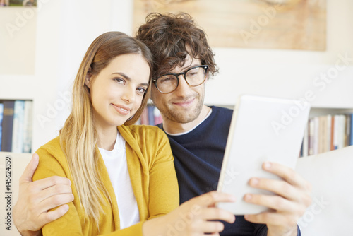 Enjoy browsing on the internet. Portrait of a lovely young couple sitting on the couch with their digital tablet at home and browsing on the internet.