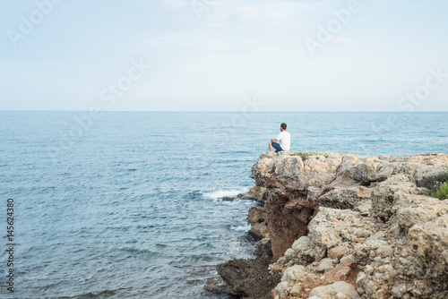 Hombre joven sentado al borde de un acantilado al atardecer. Mar Mediterr  neo