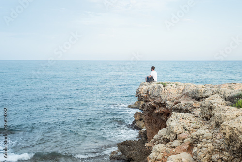 Hombre joven sentado al borde de un acantilado al atardecer. Mar Mediterr  neo