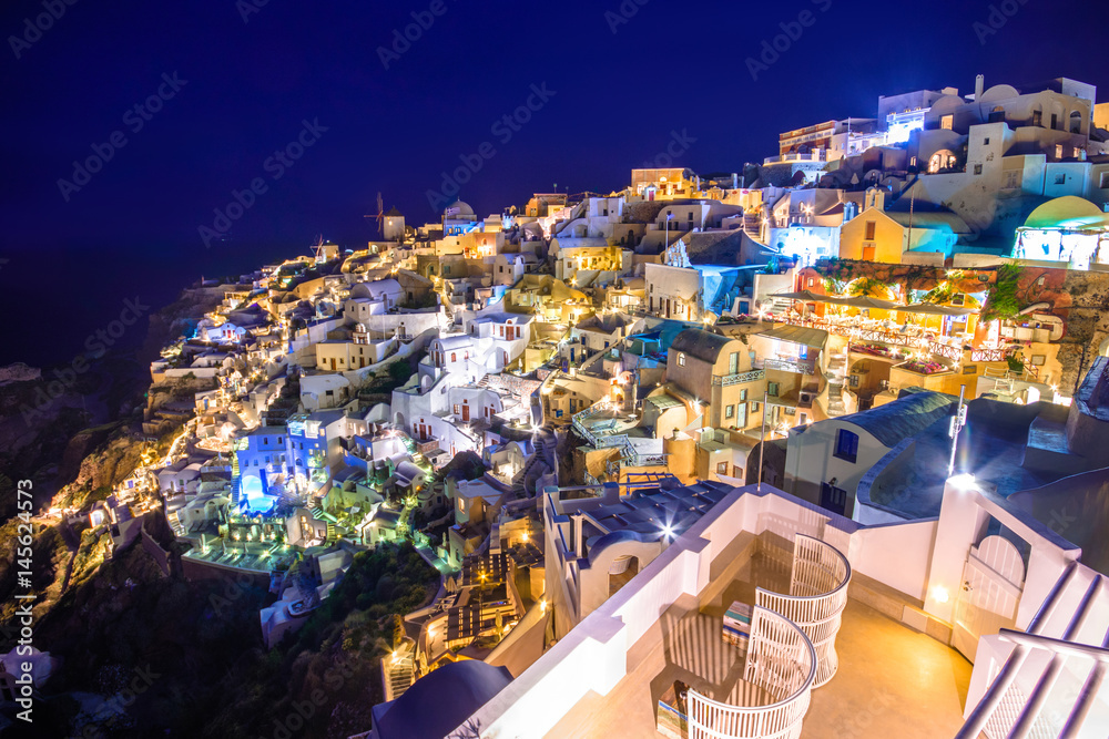 Oia town on Santorini island at night, with lights, Greece. Traditional and famous houses and churches with blue domes over the Caldera, Aegean sea