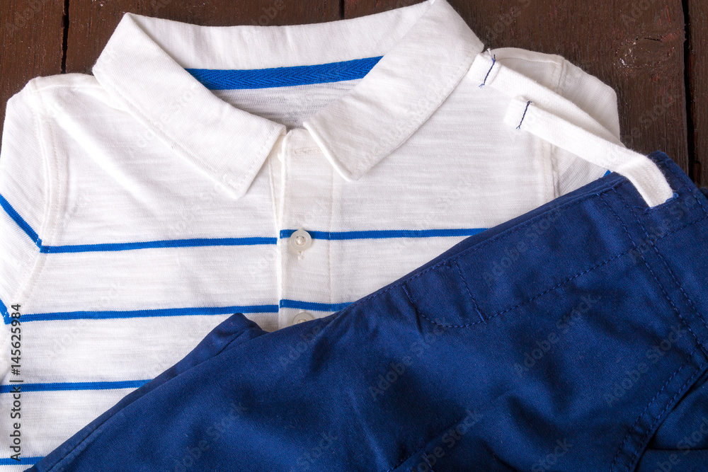 Blue shorts and white striped polo on brown wooden background. Boy outfit. Top view.