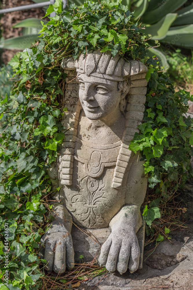Statue of an Egyptian style half man half animal in a garden with ivy growing around it