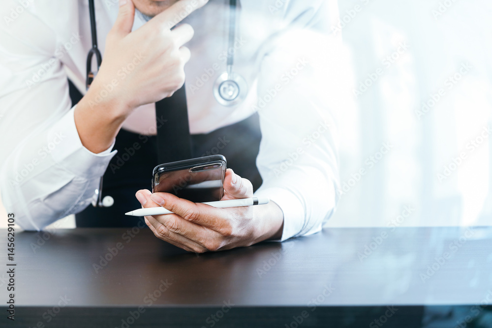 close up of smart medical doctor working with smart phone and stethoscope on dark wooden desk with glass reflected view