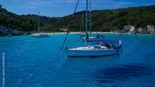 Island of Antipaxos with turquoise water and floating sailing ships