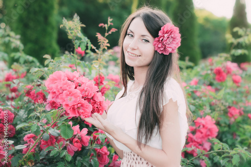Красивая девушка с длинными волосами стоит рядом с розовыми розами в саду