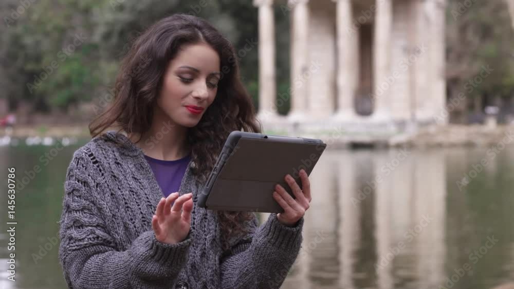 smiling gorgeus brunette uses the tablet at the park, lake in the background smiling gorgeus brunette uses the tablet at the park, lake in the background