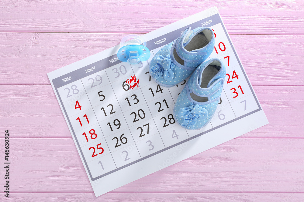 Fototapeta premium Calendar with baby booties on wooden background