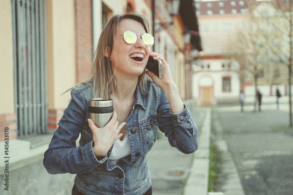 Fototapeta premium Beautiful blonde young woman walking on the street, talking on phone
