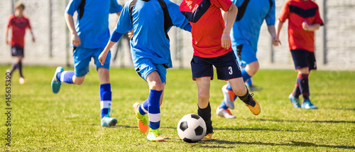 Young Boys Soccer Players Kicking Football on the Sports Field. Running Footballers in Blue and Red Jersey Shirts. Youth Soccer Horizontal Background