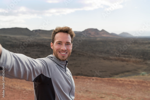 Travel tourist man taking selfie picture with smartphone hiking in volcano mountains of Lanzarote, Canary islands. Nature destination, Timanfaya National Park is a Spanish national park. photo