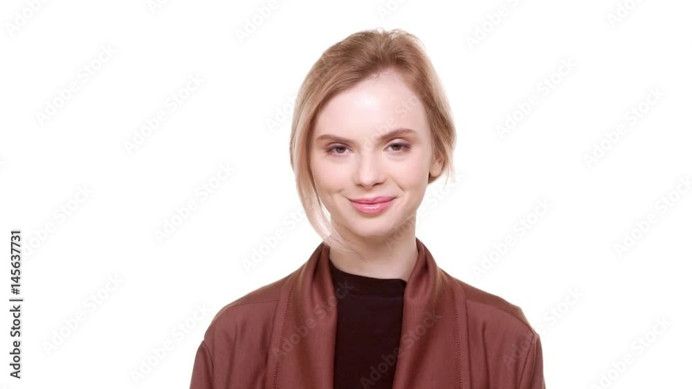 Young teenager beautiful girl standing on white background and smiling at camera in slowmotion Young teenager beautiful girl standing on white background and smiling at camera in slowmotion