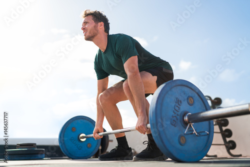 Weightlifting fitness man bodybuilding or powerlifting at outdoor gym. Bodybuilder doing barbell weight workout deadlift with heavy bar.