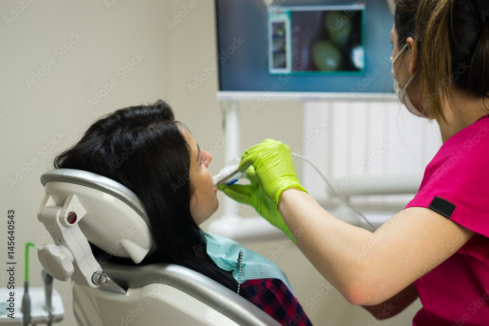 Dentist at work examining woman's teeth in dental clinic with remote
