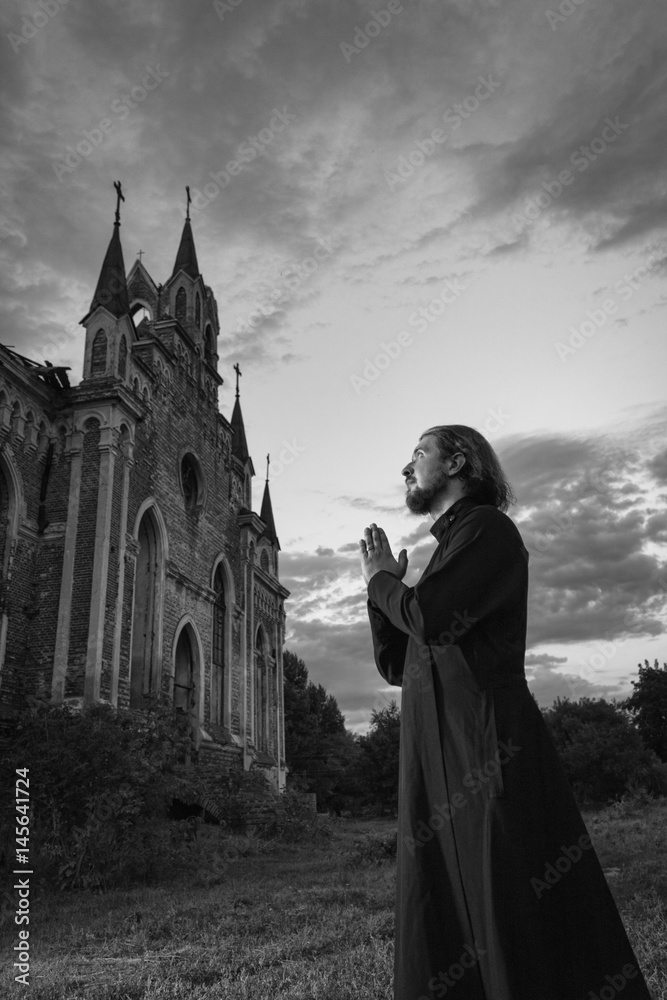 Priest during evening prayer near an old church, night scene, black and white