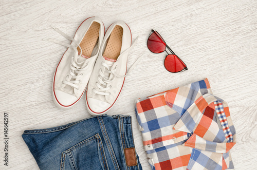 Bright checkered shirt, glasses, sneakers and jeans. Wooden background. Fashionable concept