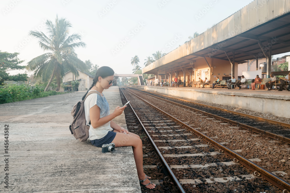 Sri Lanka. Hikkaduwa. Girl tourist with the phone in her hands crouched on the edge of the platform in anticipation of the train