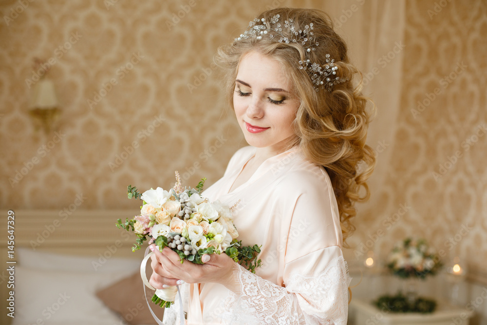 Pretty young Bride. Blonde woman with luxurious long curly hair. Boudoir morning of the bride. Taking wedding bouquet in her hands Pretty young Bride. Blonde woman with luxurious long curly hair. Boudoir morning of the bride. Taking wedding bouquet in her hands