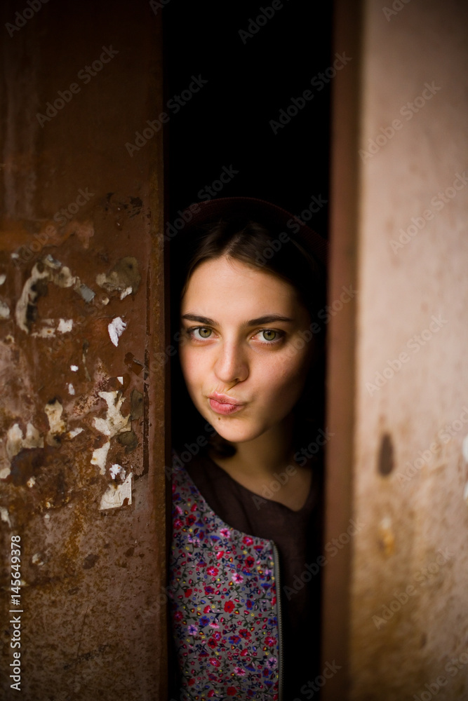 Fototapeta premium A young curious girl looks out from behind the door of her house. She thinks about going outside. agoraphobia concept