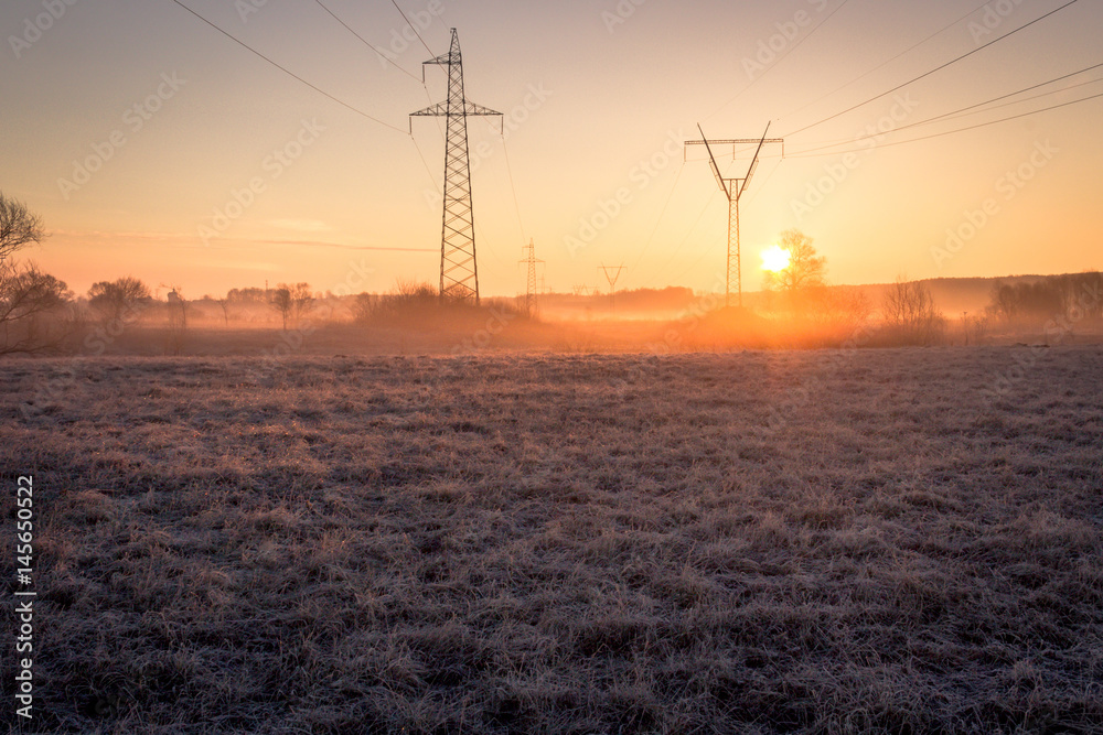High voltage line supports in fog at frosty spring sunrise morning
