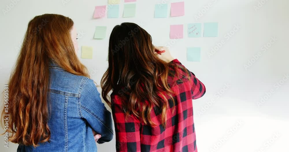 Rear view of female executives writing on sticky notes Rear view of female executives writing on sticky notes