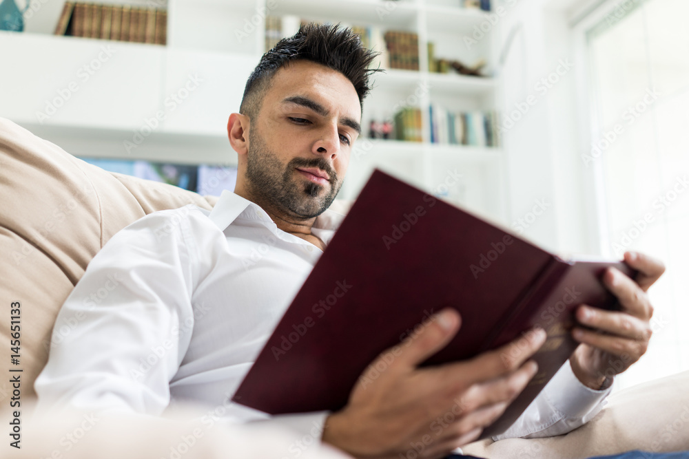 Obraz premium Young confident man reading book at modern home