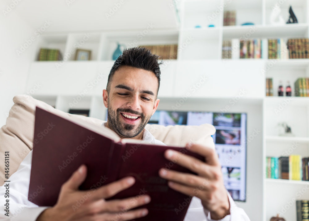 Fototapeta premium Young confident man reading book at modern home