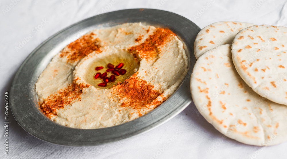 Hummus with paprika, olive oil, and pomegranate seeds against white background. Selective focus.