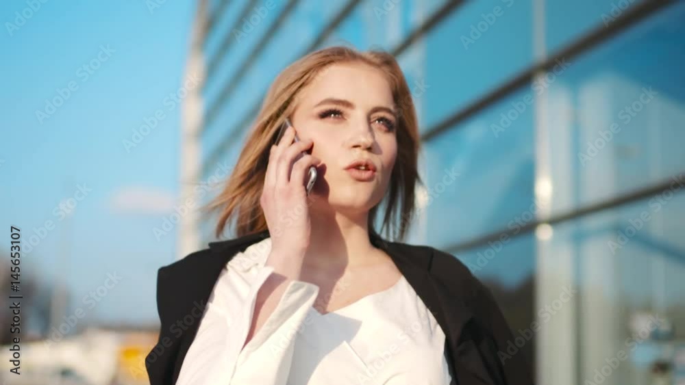Gorgeous stylish young woman in an elegant outfit passing the airport terminal and talking on the phone. Sunny weather, being a boss. Successful life.