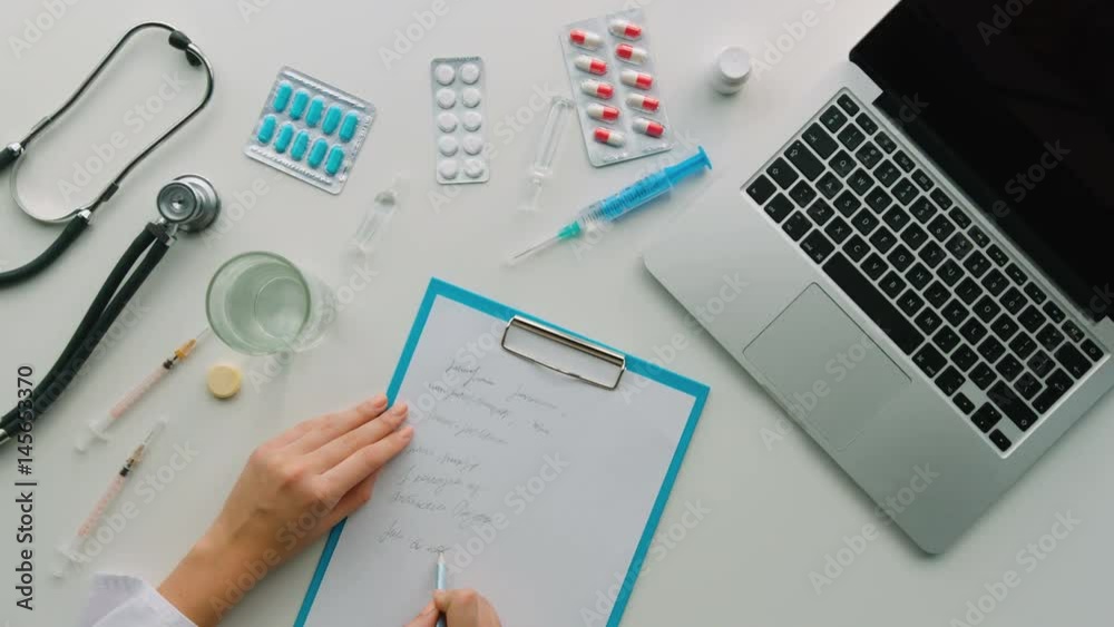 Young woman make some medical notes in notebook from here laptop. Top View. White background. Young woman make some medical notes in notebook from here laptop. Top View. White background.