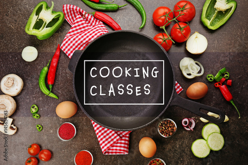 Empty frying pan on napkin with fresh ingredients and spices on dark background, top view photo