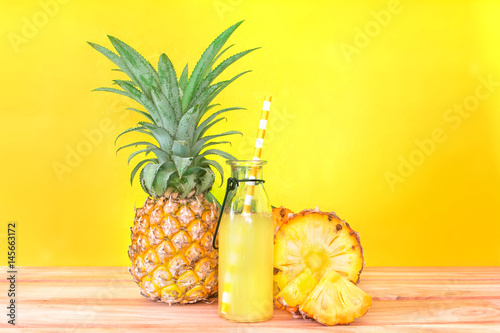The Bottles of pineapple juice with sliced pineapple fruit on wooden table with vibrant yellow background , summer fruit drink concept