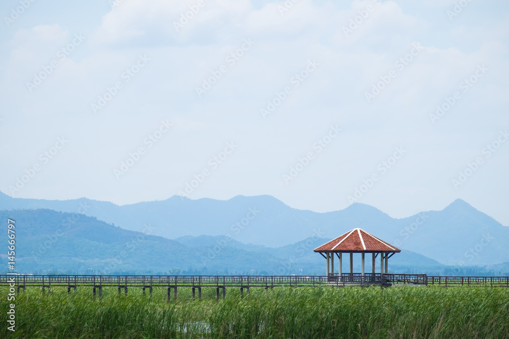 Small Pavillion on wooden bridge in swamp with grass field with blue sky mountain range background. Khao Sam Roi Yot National Park, Prachuap Khiri Khan, Thailand.