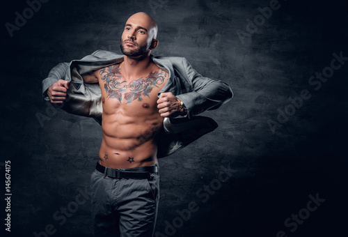 Shaved head tattooed male dressed in a grey jacket on a naked torso. © Fxquadro
