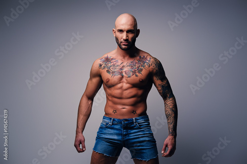 Fototapeta Shaved head, muscular male with tattoos on his torso over grey vignette background