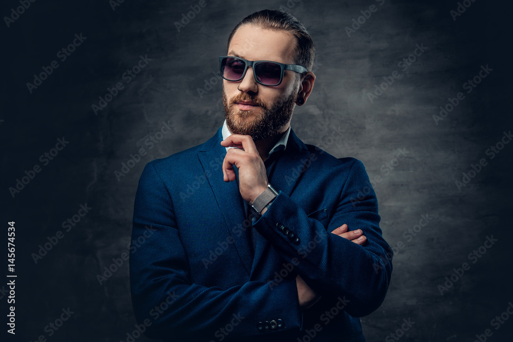 A stylish bearded male dressed in a suit and sunglasses over dark grey background. A stylish bearded male dressed in a suit and sunglasses over dark grey background.