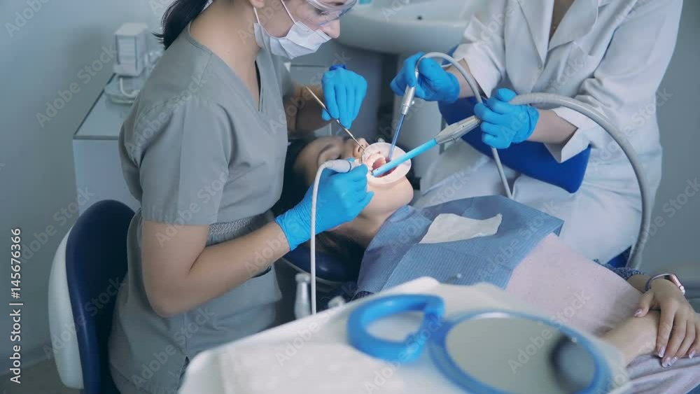 Young woman sitting in dental chair. Doctor with dental nurse treating a patient, scaling and polishing the teeth. Young woman sitting in dental chair. Doctor with dental nurse treating a patient, scaling and polishing the teeth.