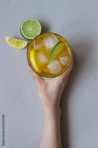Hand holding ice drink with lemon and lime on the light blue background, top view